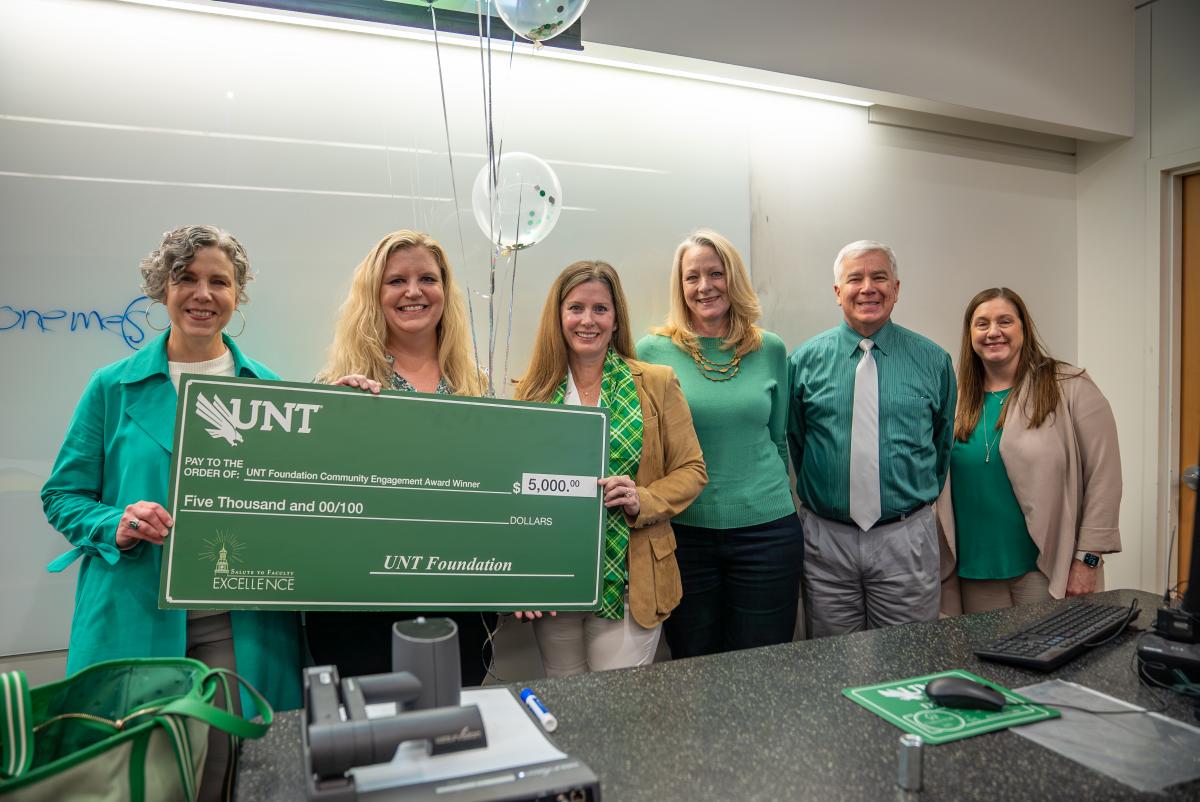 Lauren Mathews posing with giant award check during class visit from UNT administrators and Board CEO