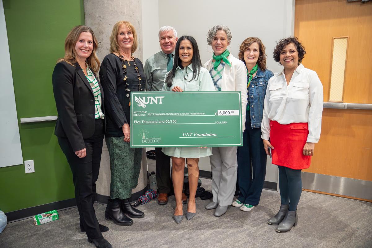Marissa Zorola posing with giant award check during class visit from UNT administrators and Foundation CEO